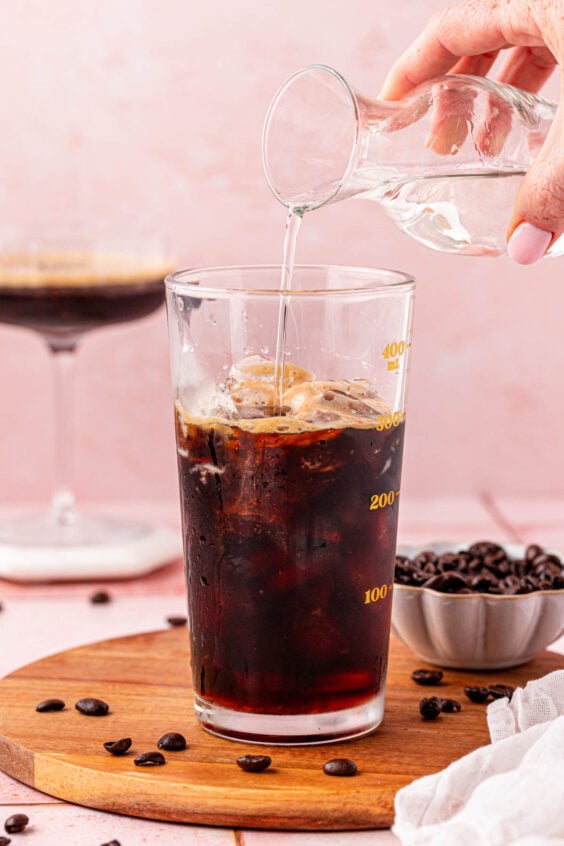 Simple syrup being added to a cocktail shaker with espresso.