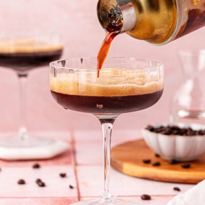 A drink shaker pouring a non alcoholic espresso martini in a coupe glass.