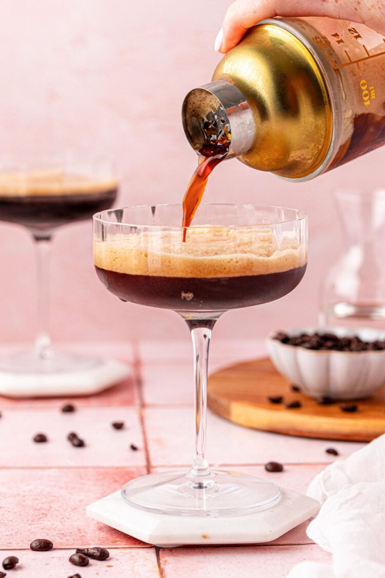 A drink shaker pouring a non alcoholic espresso martini in a coupe glass.