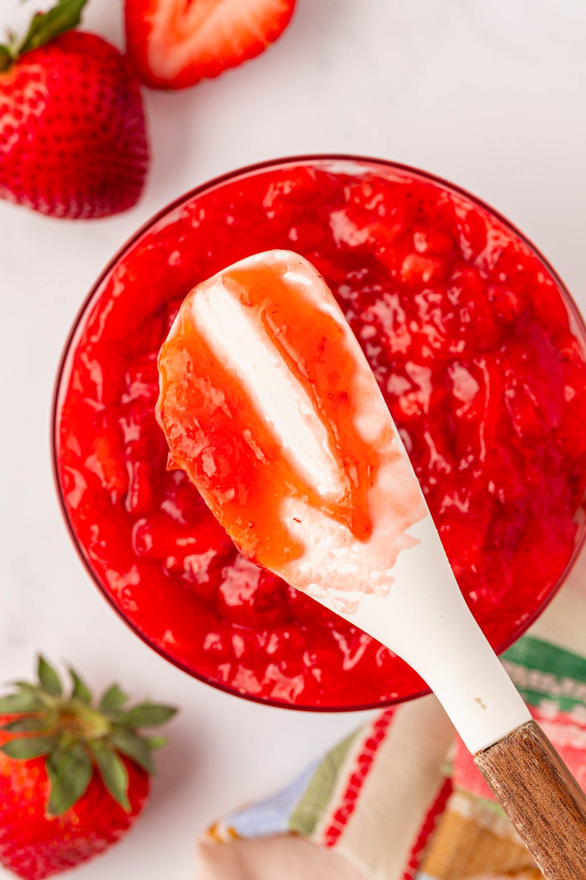 Overhead photo of a rubber spatula with strawberry filling on it and in a bowl under it.