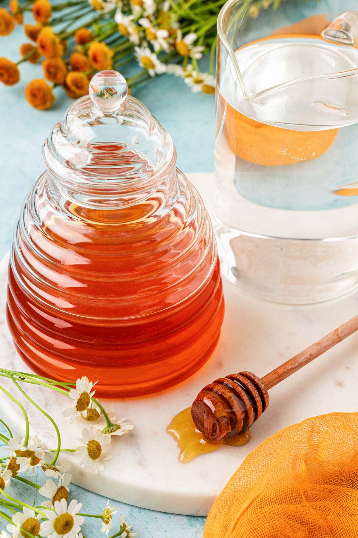 A glass of water and a glass container of honey on a table.