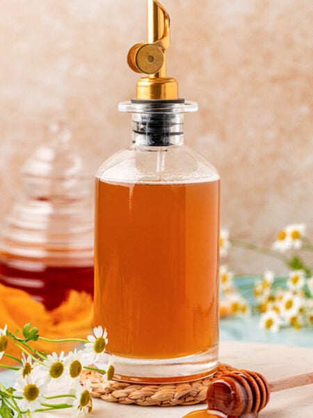 A glass bottle of honey simple syrup on a rope coaster.