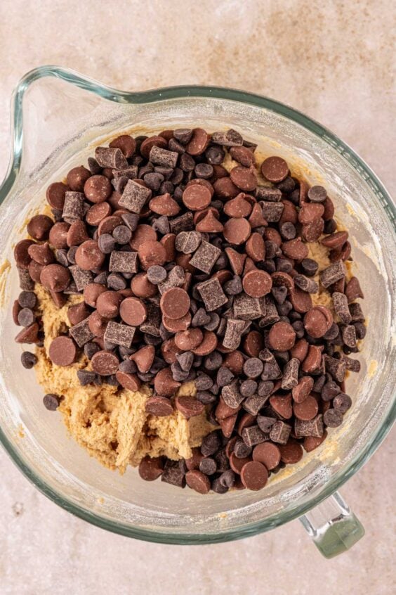 Chocolate chips and chunks being added to cookie dough in a mixing bowl.