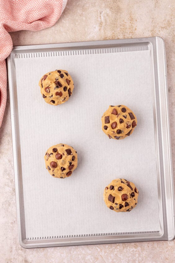 Baking sheet lined with parchment paper with 4 cookie dough balls on it.