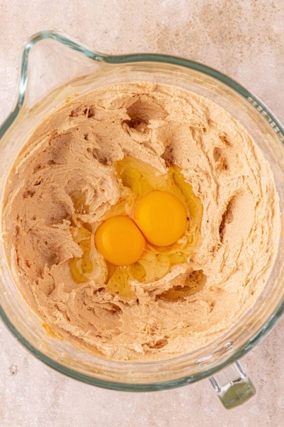 Two eggs being added to a mixing bowl to make cookie dough.