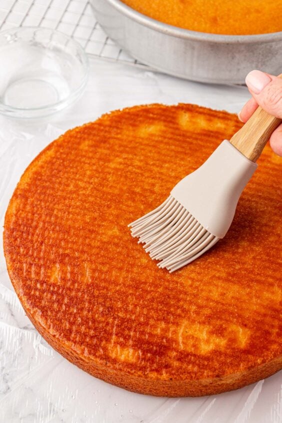 A silicone brush brushing vanilla cake with simple syrup.