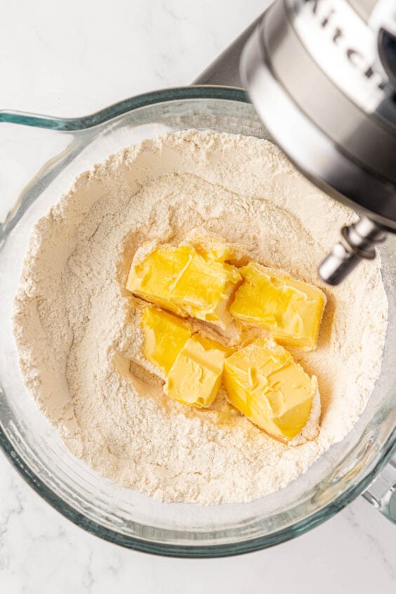 Softened butter being added to flour and sugar in a mixing bowl.
