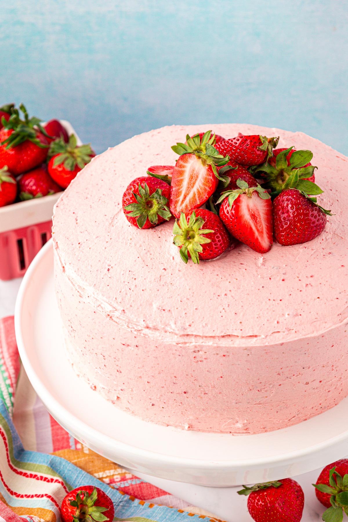 Close up of a strawberry frosted cake on a white cake stand.