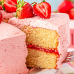 A slice of strawberry cake being lifted off a white cake stand.