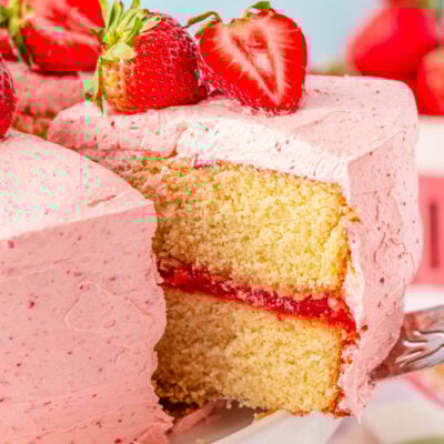 A slice of strawberry cake being lifted off a white cake stand.