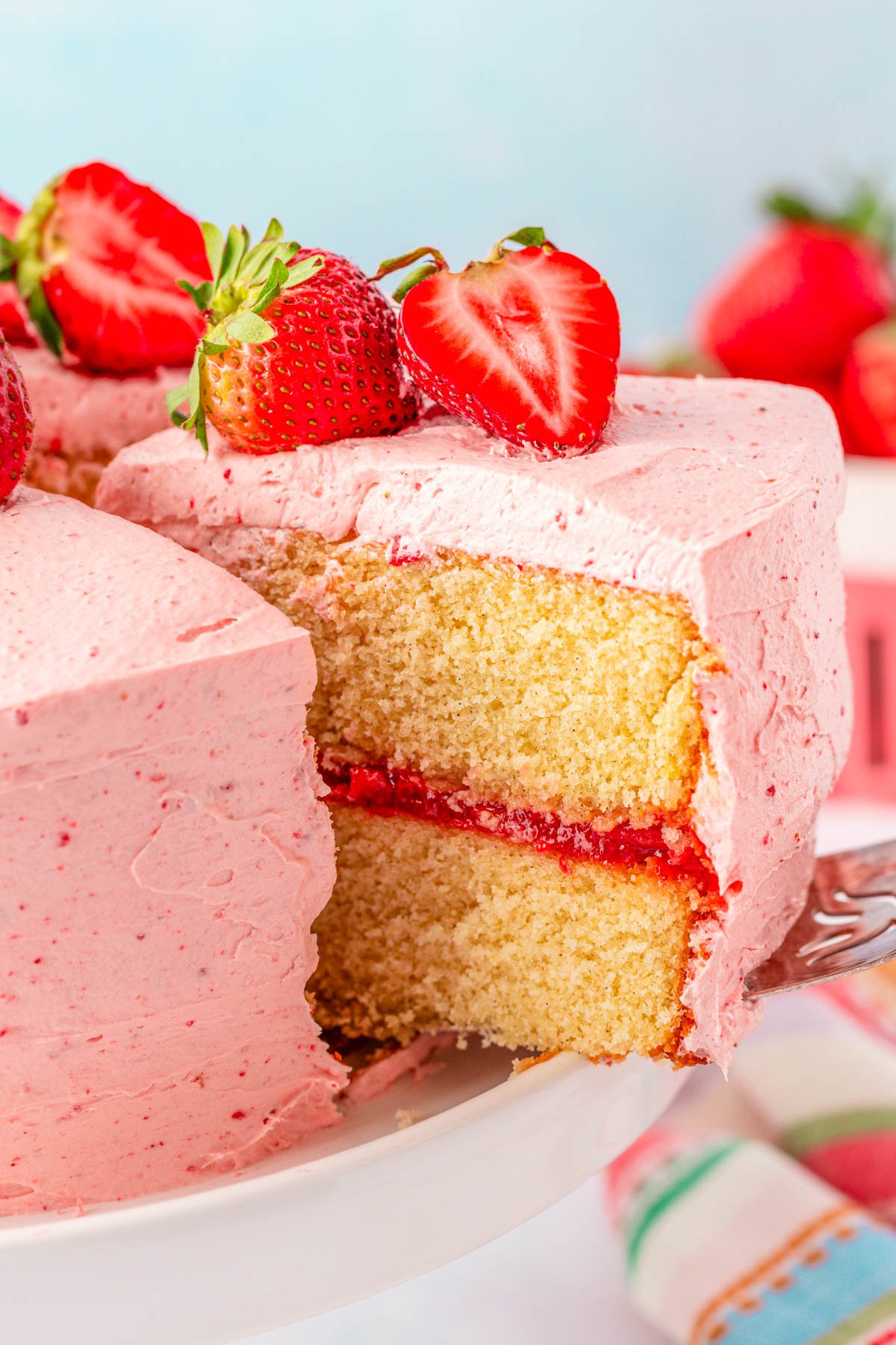 A slice of strawberry cake being lifted off a white cake stand.