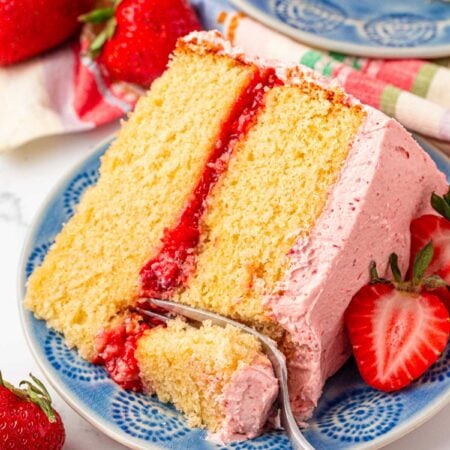 Close up photo of a slice of strawberry vanilla cake with a fork taking a bite from it.