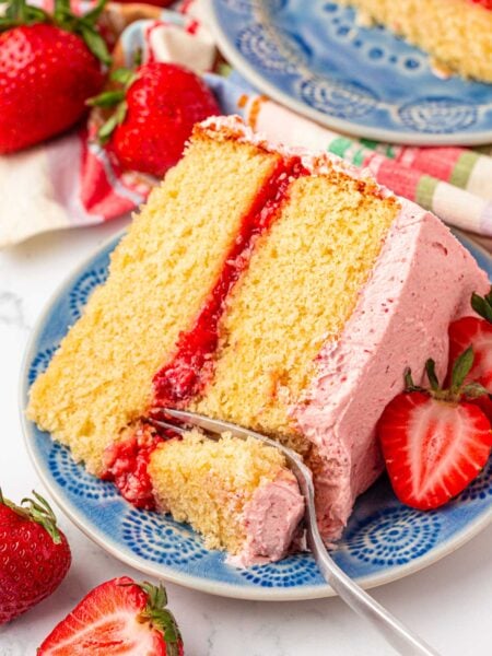 Close up photo of a slice of strawberry vanilla cake with a fork taking a bite from it.