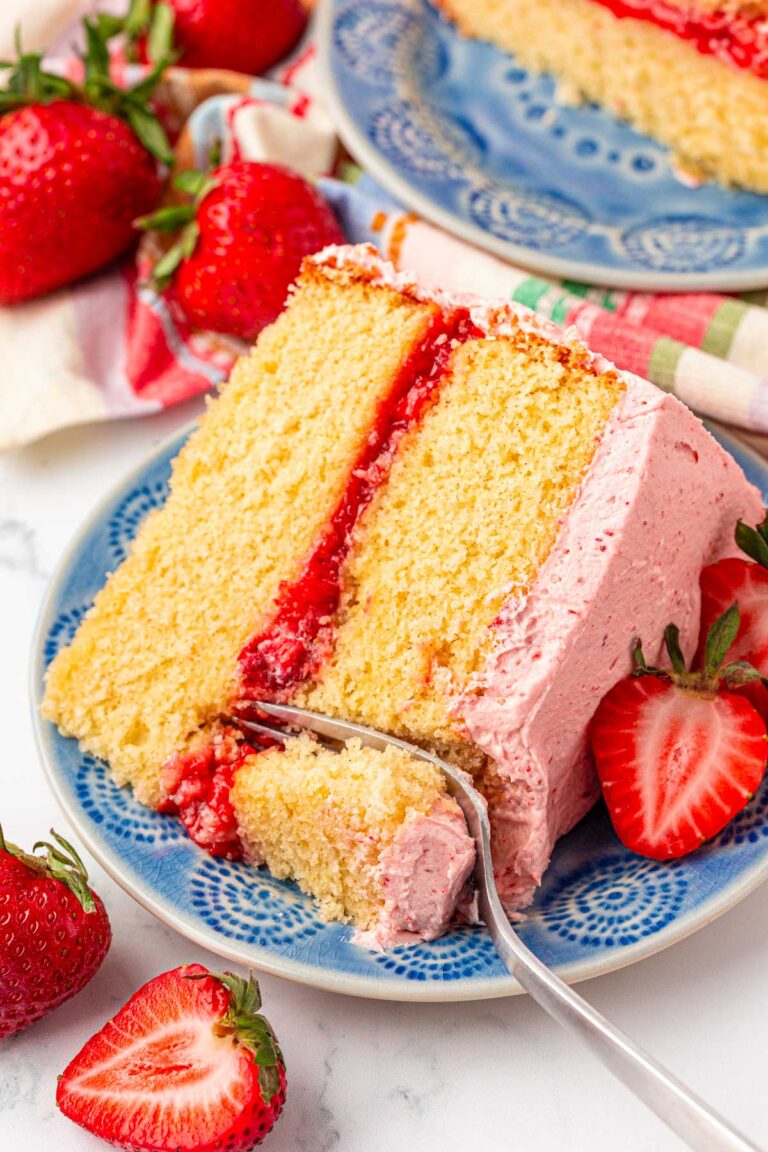 Close up photo of a slice of strawberry vanilla cake with a fork taking a bite from it.