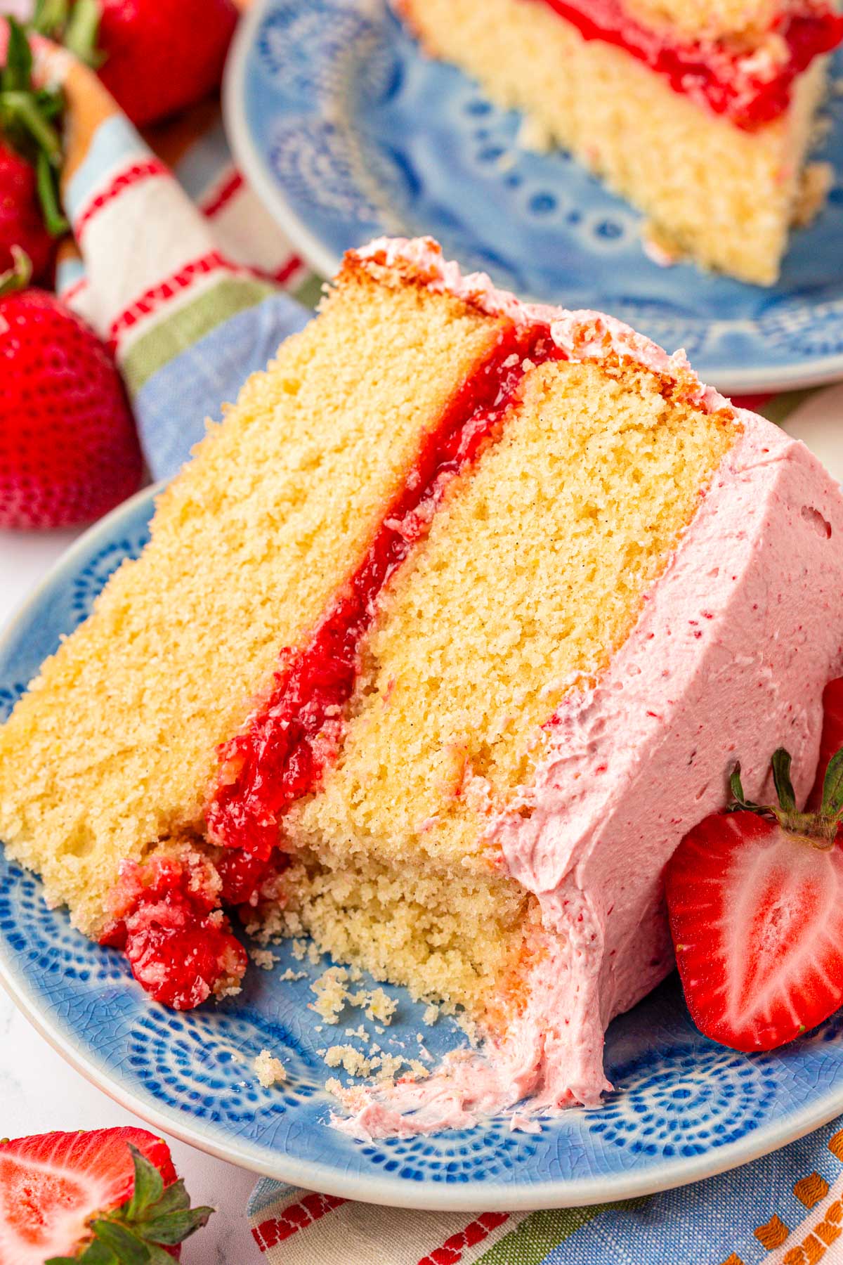 A slice of vanilla cake with strawberry frosting and filling on a blue plate.