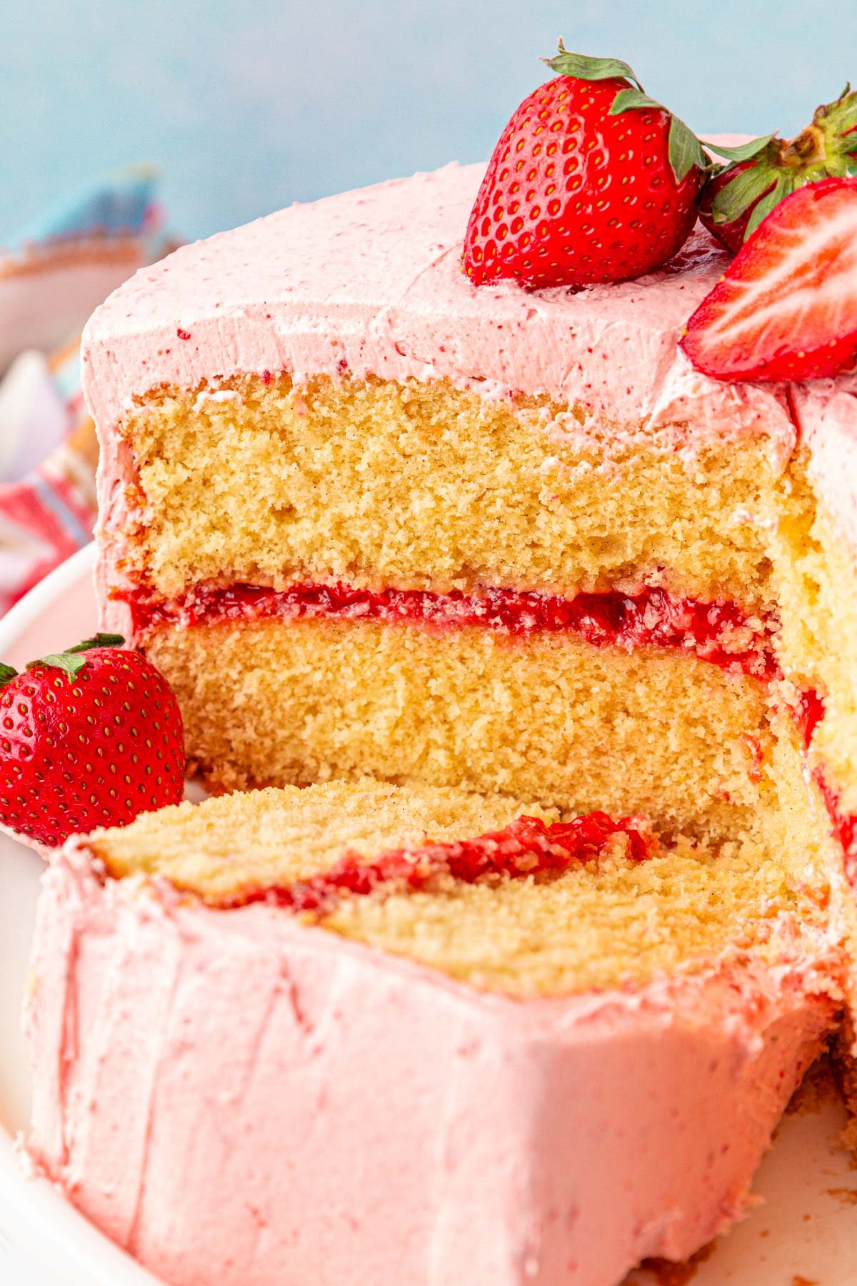 Slice of strawberry cake on a cake stand laying next to the rest of the cake.