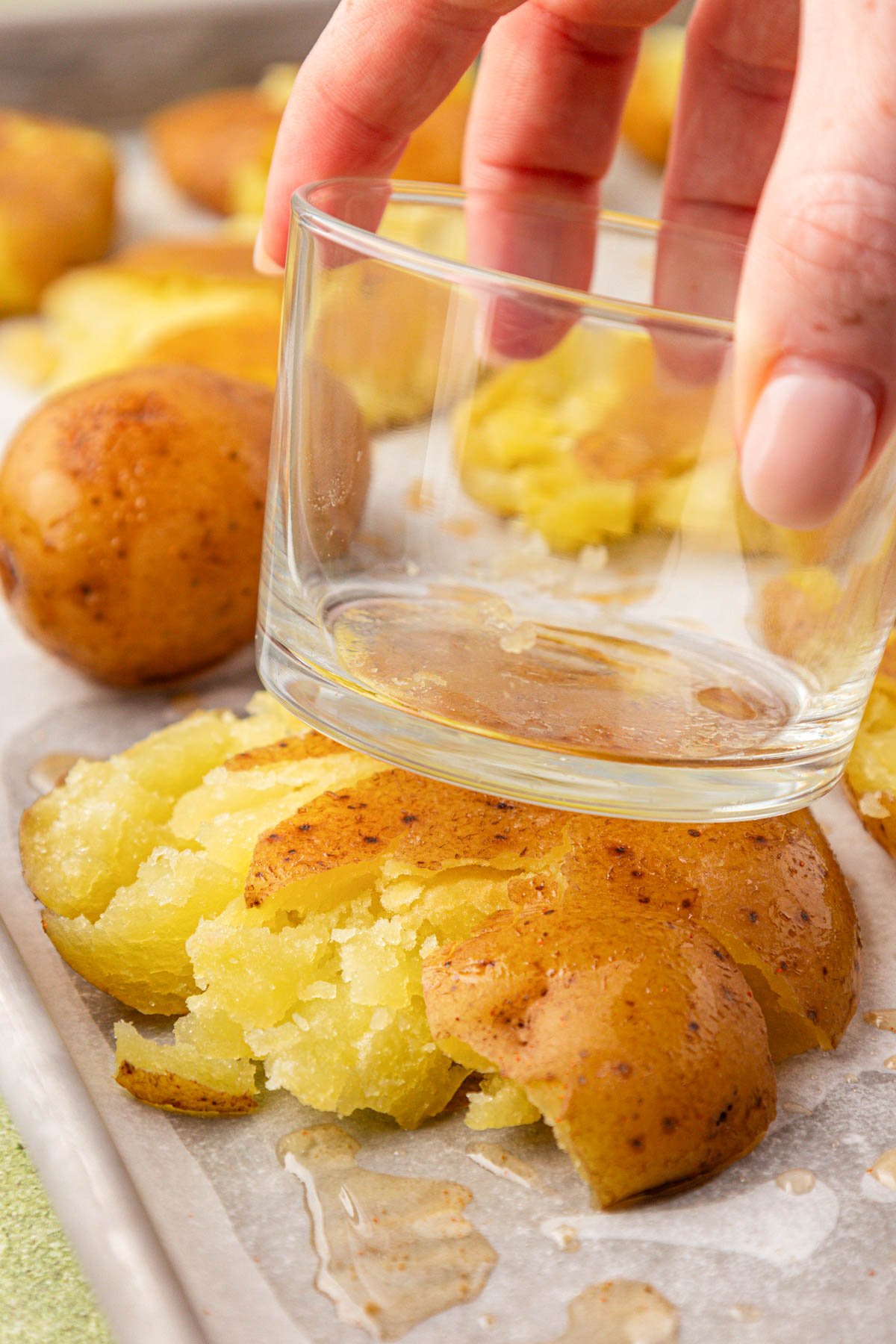 A woman's hand pressing a glass on top of a potato on a sheet pan.