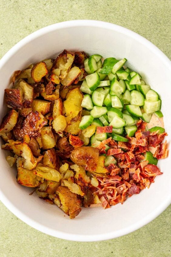 Potatoes, cucumber, and bacon in a white bowl.