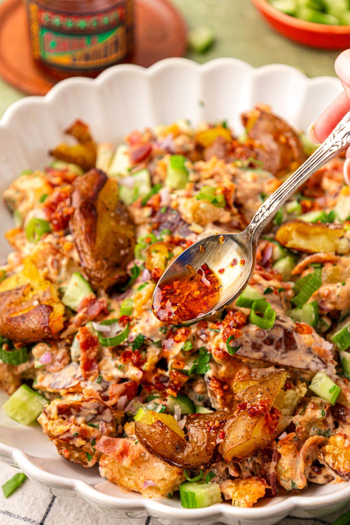 Close up of a spoon drizzling chili crisp over potato salad.