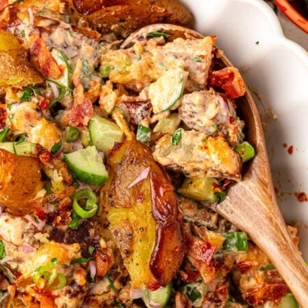 A wooden spoon in a white bowl filled with chili crisp smashed potato salad.