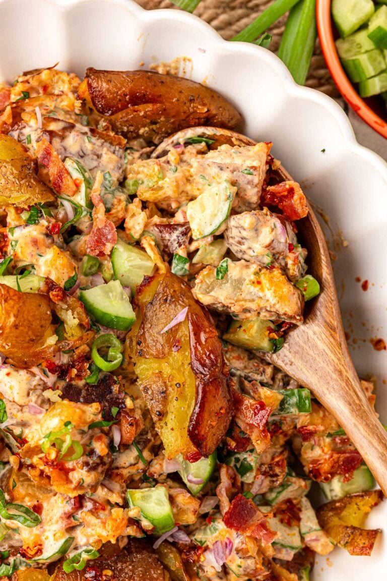 A wooden spoon in a white bowl filled with chili crisp smashed potato salad.