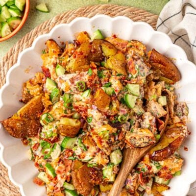 Overhead photo of a white bowl of chili crisp potato salad with a wooden serving spoon in it.