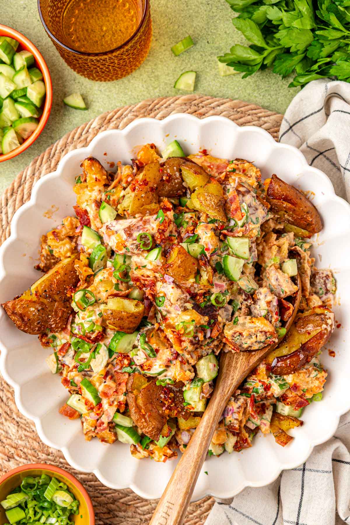 Overhead photo of a white bowl of chili crisp potato salad with a wooden serving spoon in it.