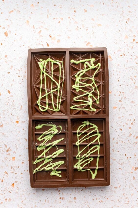 Green colored white chocolate drizzled in a chocolate bar mold.