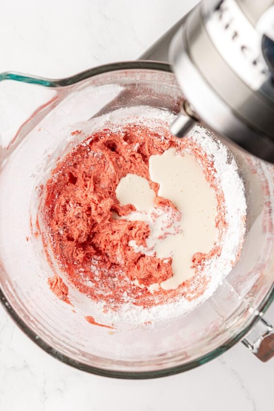 Cream is being added to the strawberry frosting.