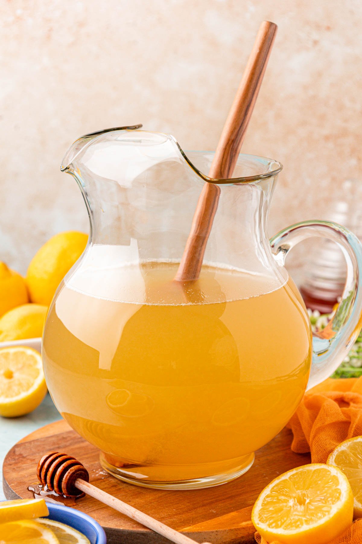 A glass pitcher with a wooden spoon in it to make lemonade with honey.