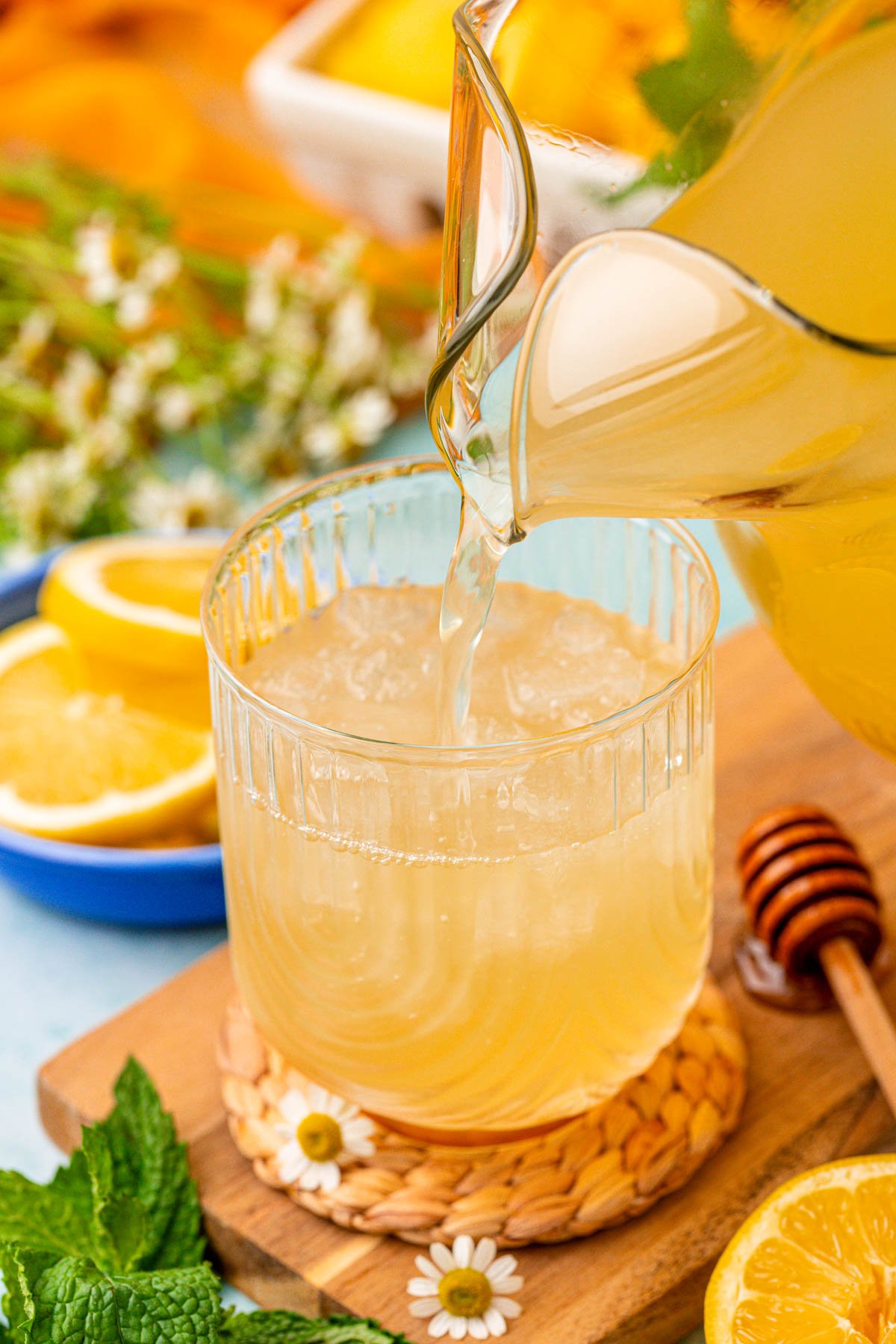 Honey lemonade being poured out of a pitcher into a glass with ice.