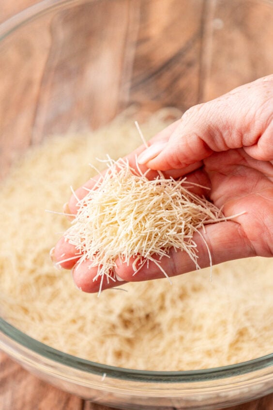 Kataifi dough being crushed into smaller pieces in a mixing bowl.