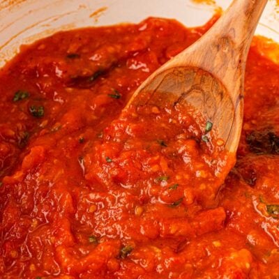 Close up of a pot of tomato sauce with a wooden spoon on it.
