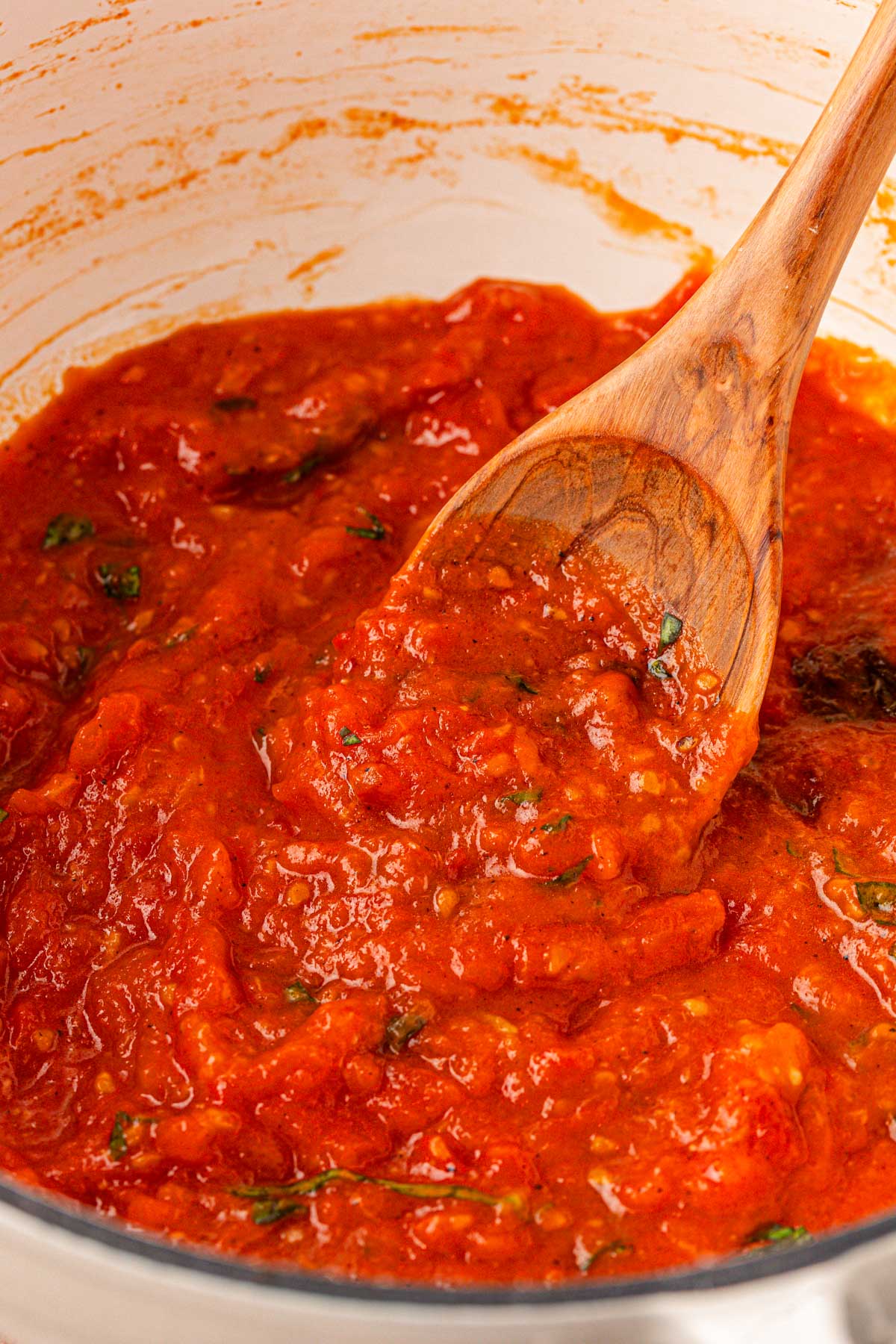Close up of a pot of tomato sauce with a wooden spoon on it.