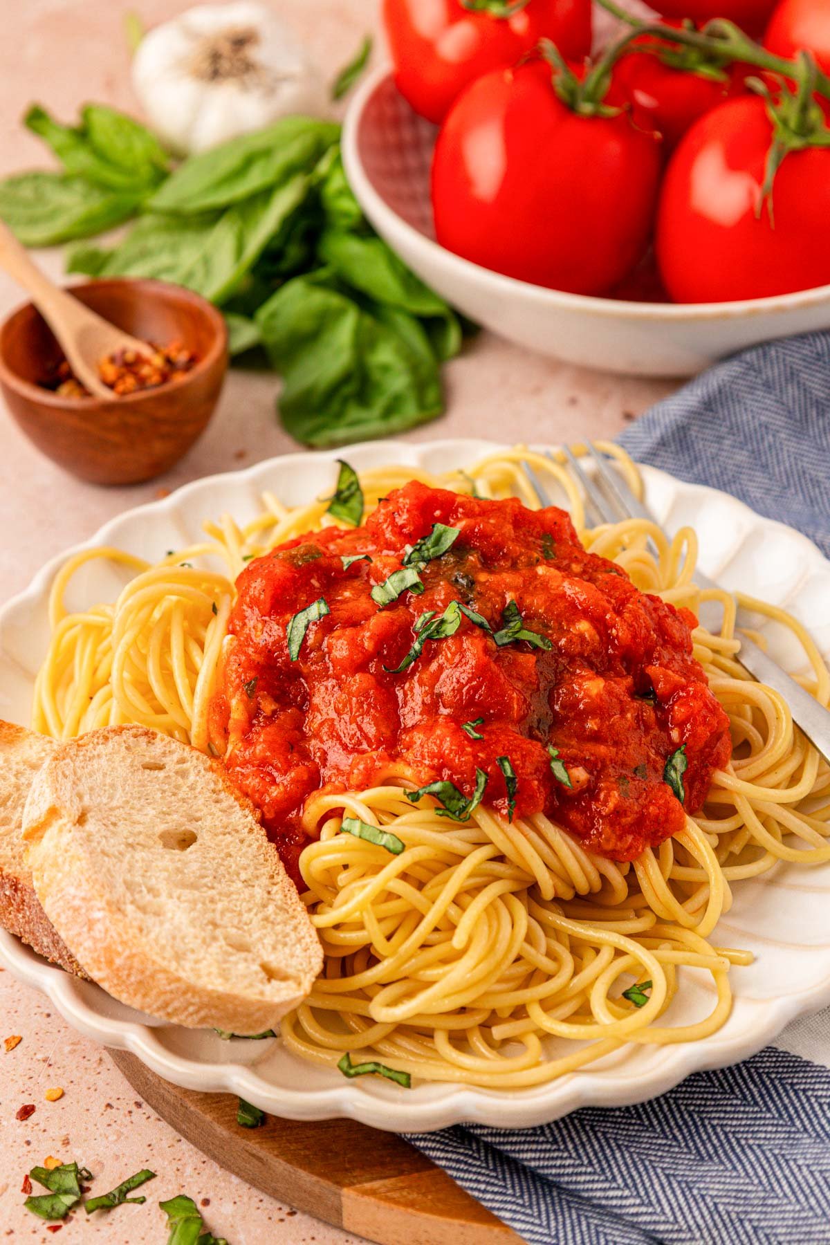 A white scalloped plate filled with spaghetti and fresh tomato sauce, and a side of bread.