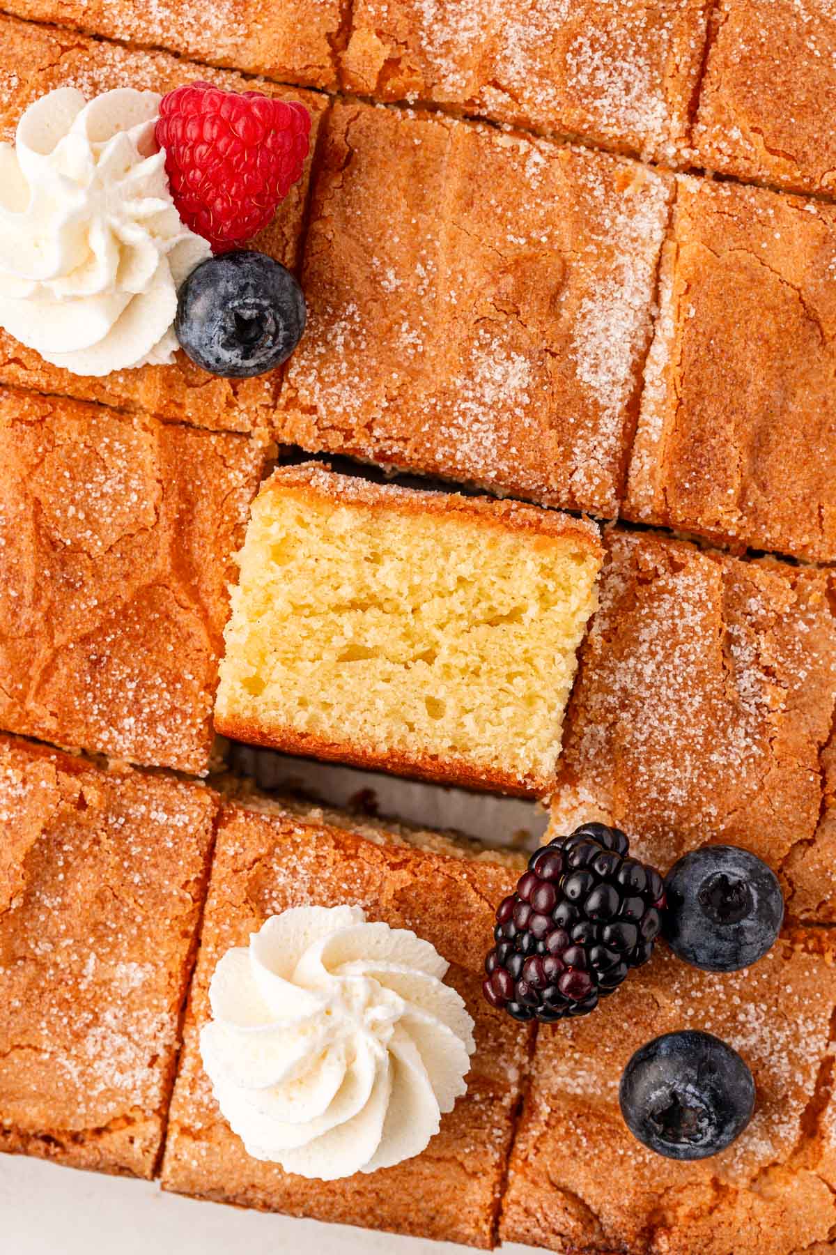 Overhead photo of a square butter cake that has been sliced and some slices are topped with whipped cream and berries.
