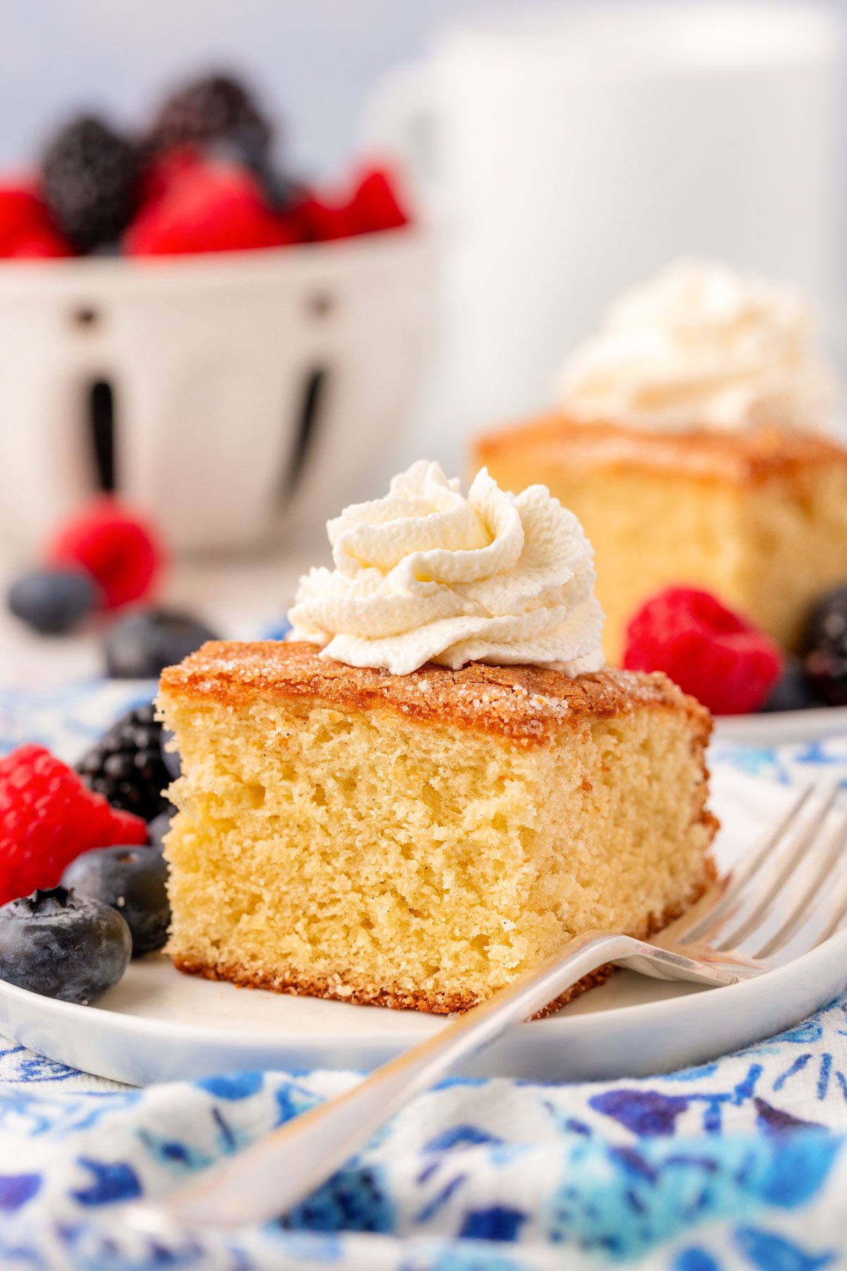 A slice of butter cake on a white plate with whipped cream on top.