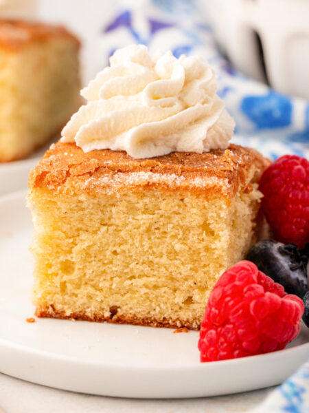 A slice of butter cake on a white plate with whipped cream and berries.