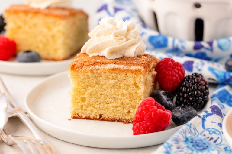 A slice of butter cake on a white plate with whipped cream and berries.
