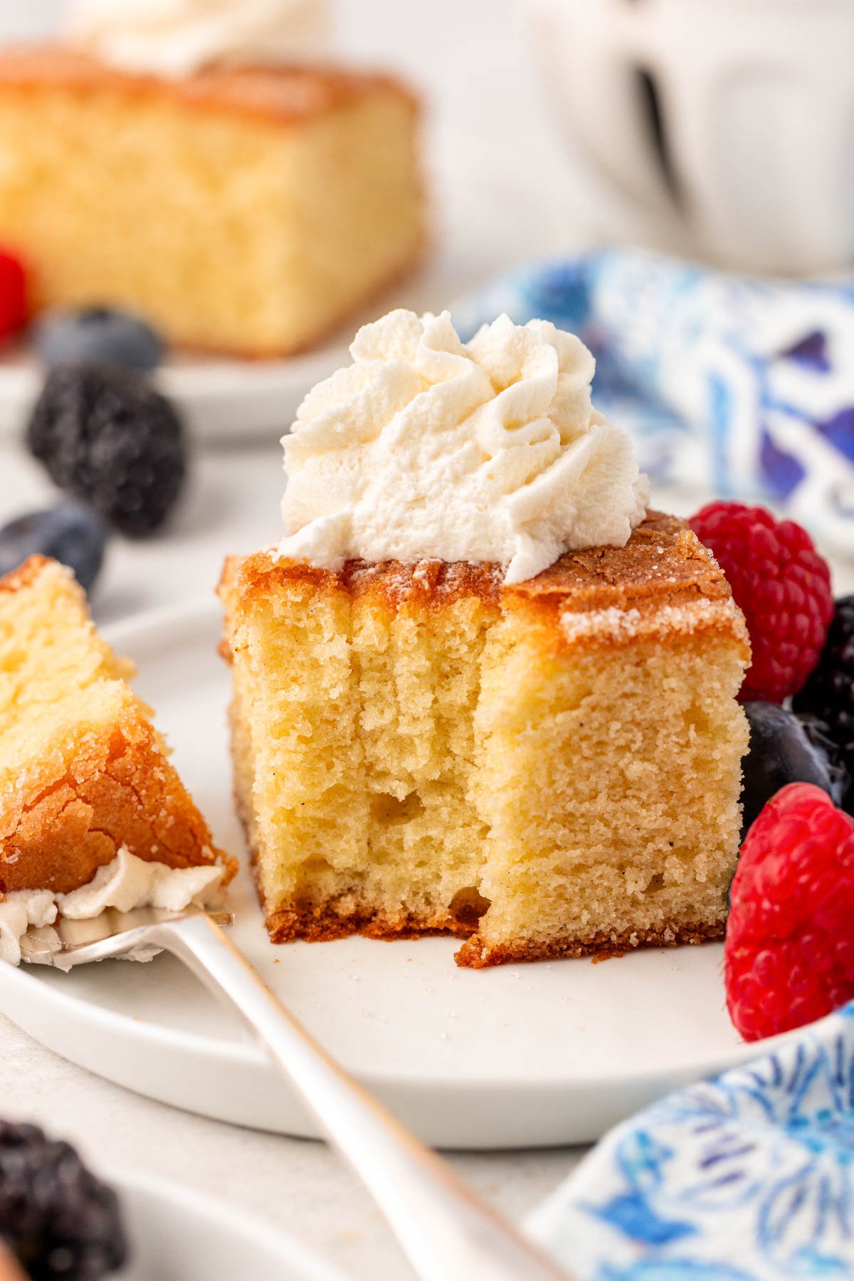 A slice of butter cake on a white plate with a bite missing from it.