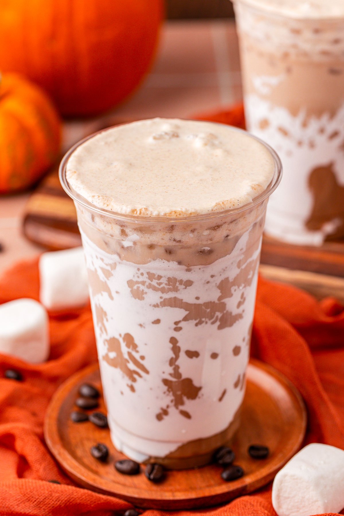 An iced fluffy pumpkin latte on a wooden coaster.