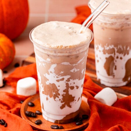 Close up of two cups of pumpkin nutella iced coffees on an orange table.