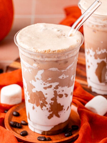 Close up of two cups of pumpkin nutella iced coffees on an orange table.