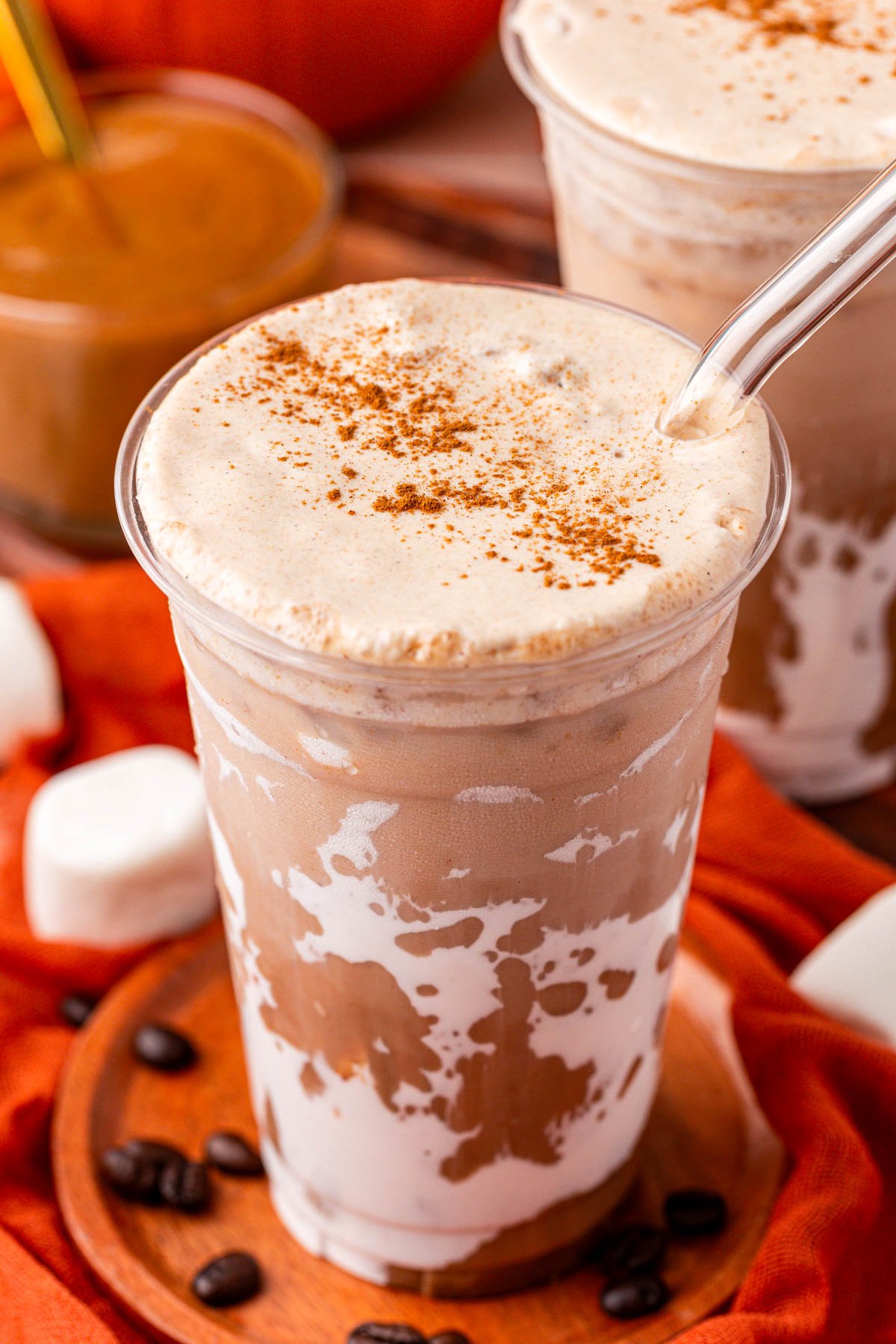 A large plastic cup of a fluffy pumpkin latte on a wooden coaster.