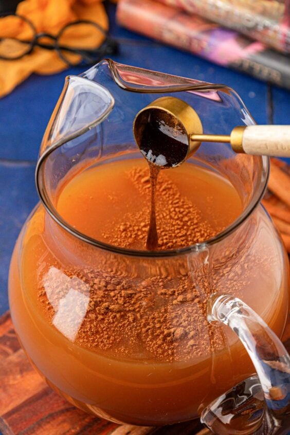 Vanilla bean paste being added to a pitcher of pumpkin juice.