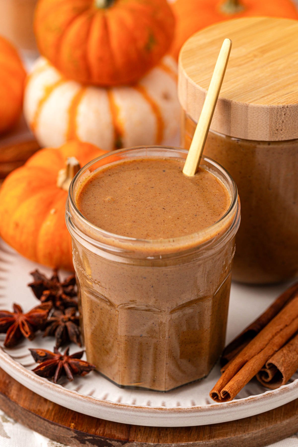 A jar of pumpkin spice coffee sauce on a plate with spices and pumpkins.