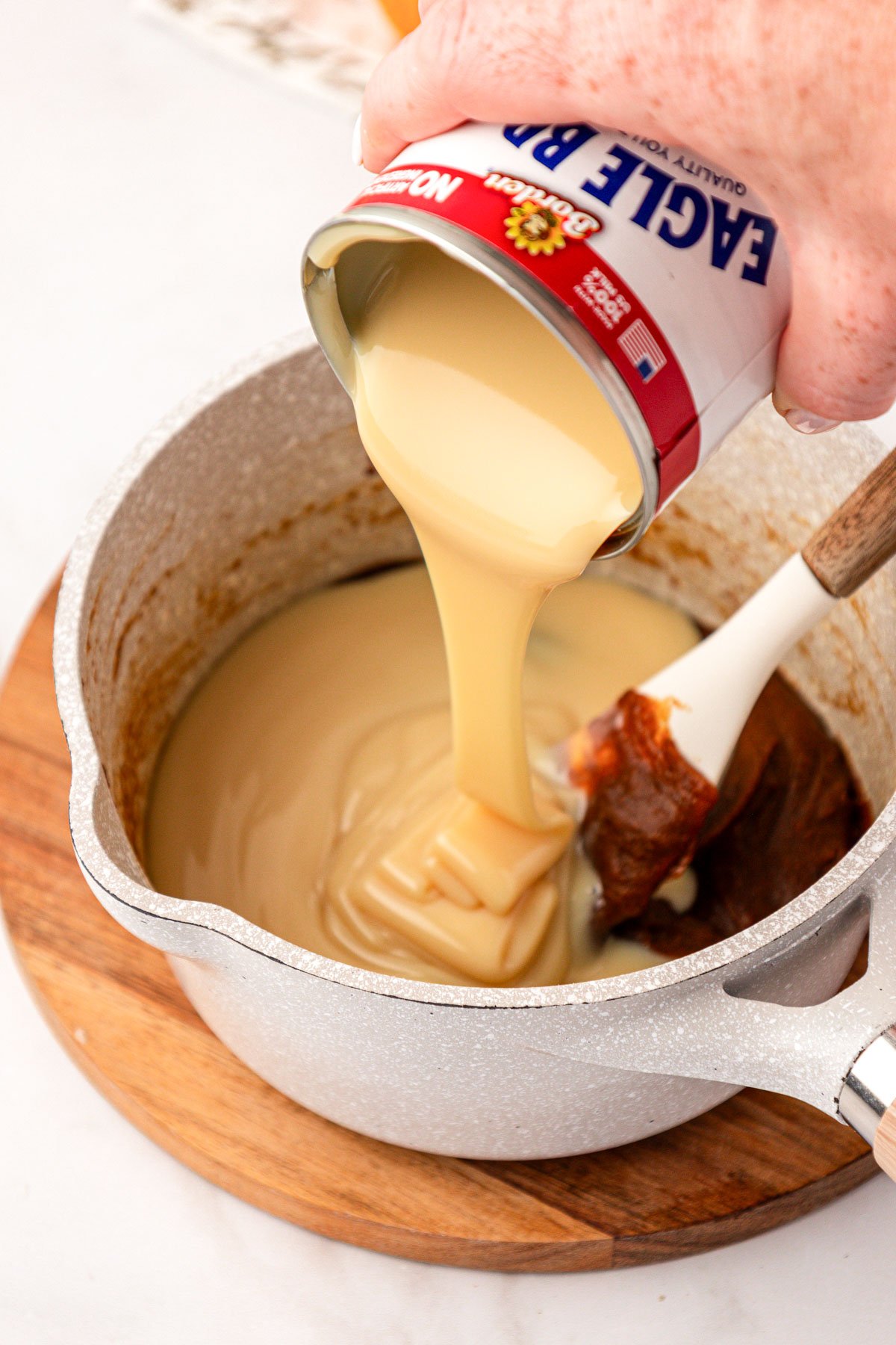 Sweetened condensed milk being poured into a pot of pumpkin puree to make sauce.