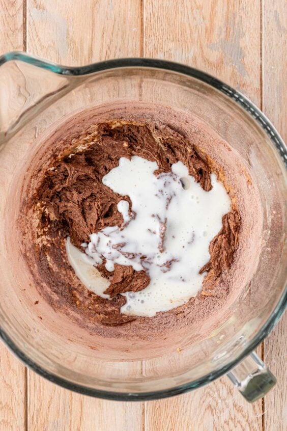 Buttermilk being added to chocolate cake batter in a mixing bowl.