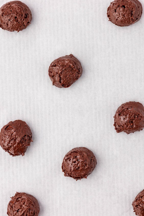 Mounds of chocolate cake batter to make whoopie pies on parchment paper.