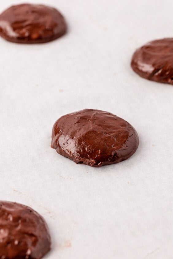 Mounds of chocolate cake batter to make whoopie pies on parchment paper.